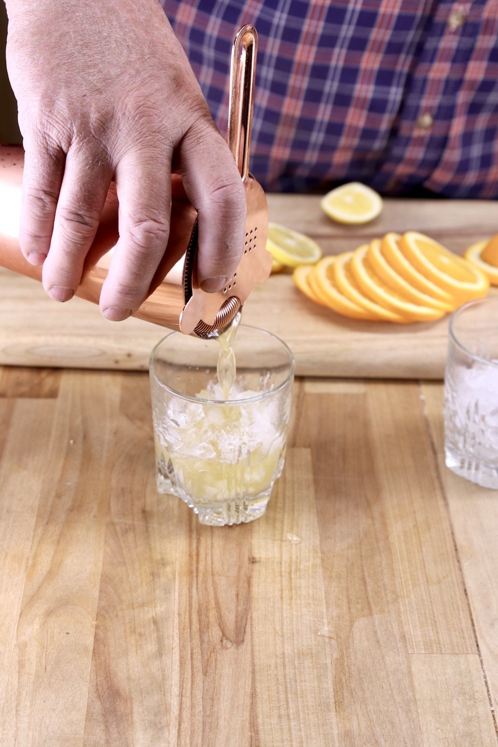 Straining amaretto whiskey sour cocktail into an old fashioned glass with crushed ice