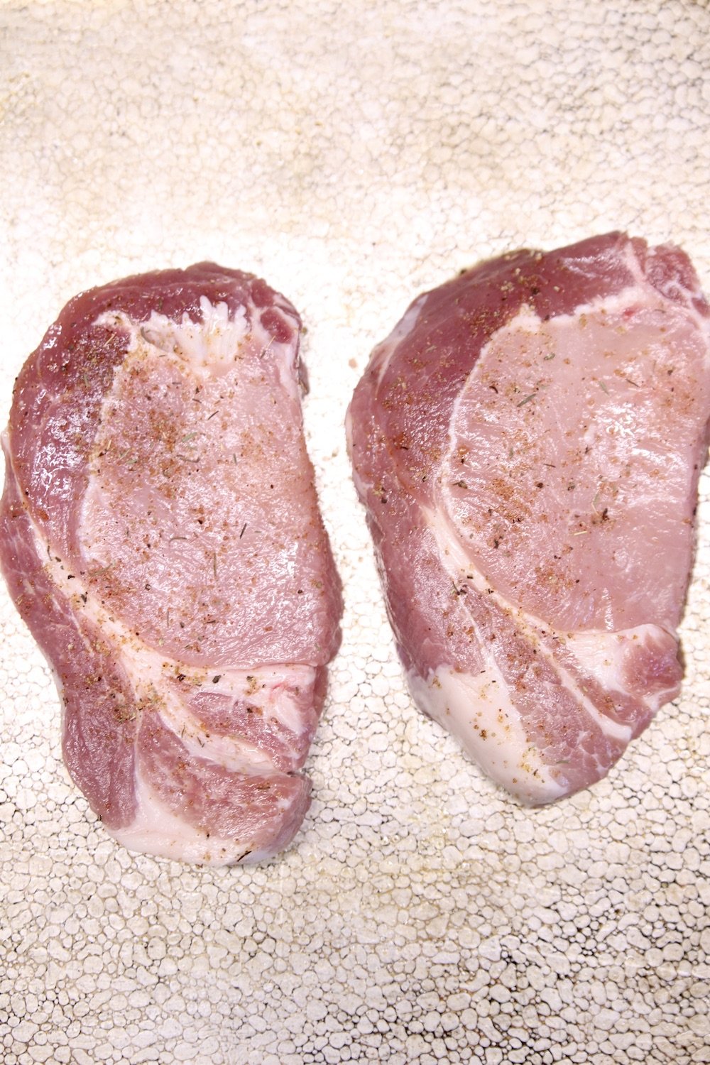 pork chops on a baking sheet seasoned with salt and pepper