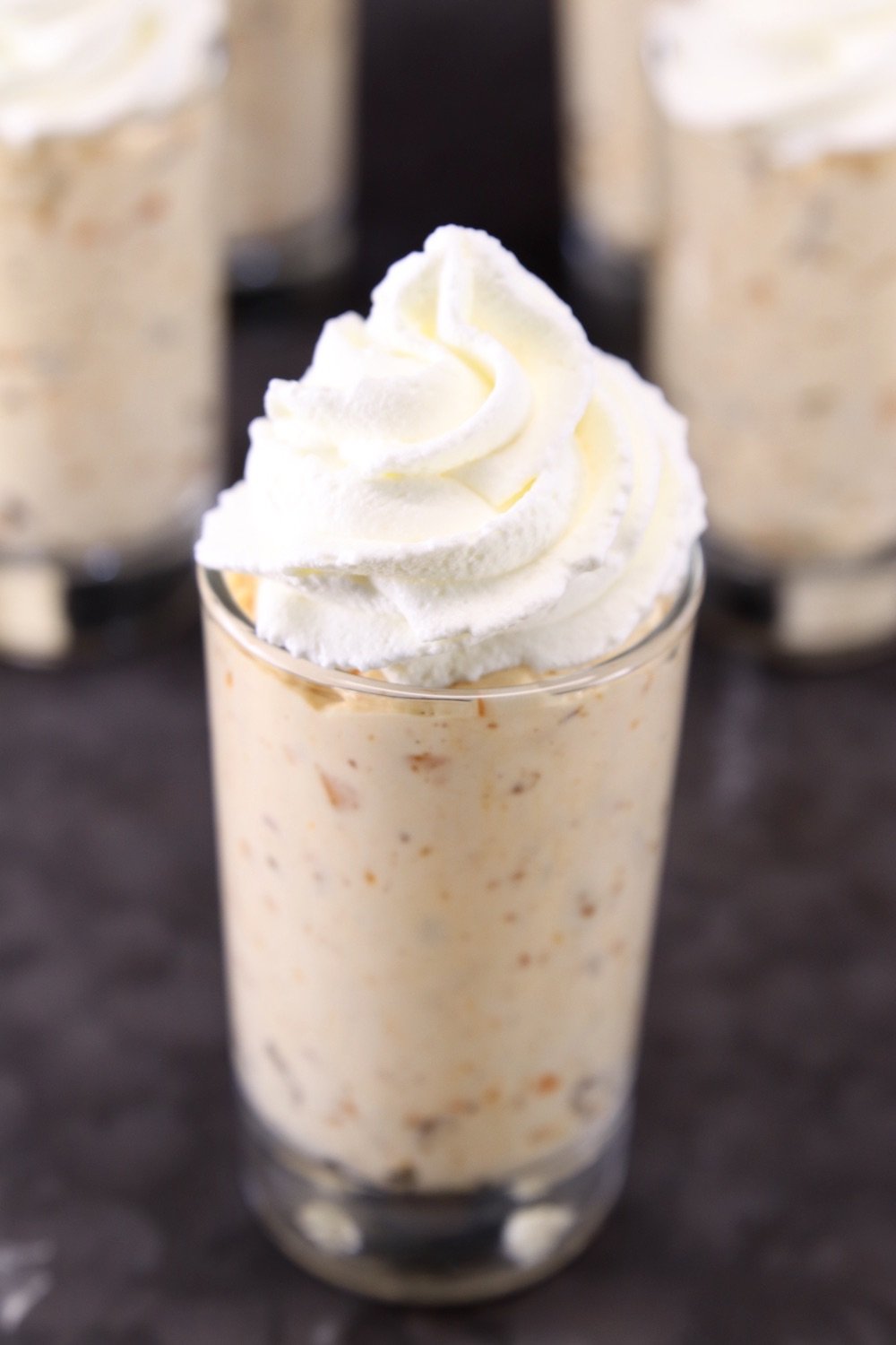 Butterfinger cheesecake in a juice glass topped with whipped cream