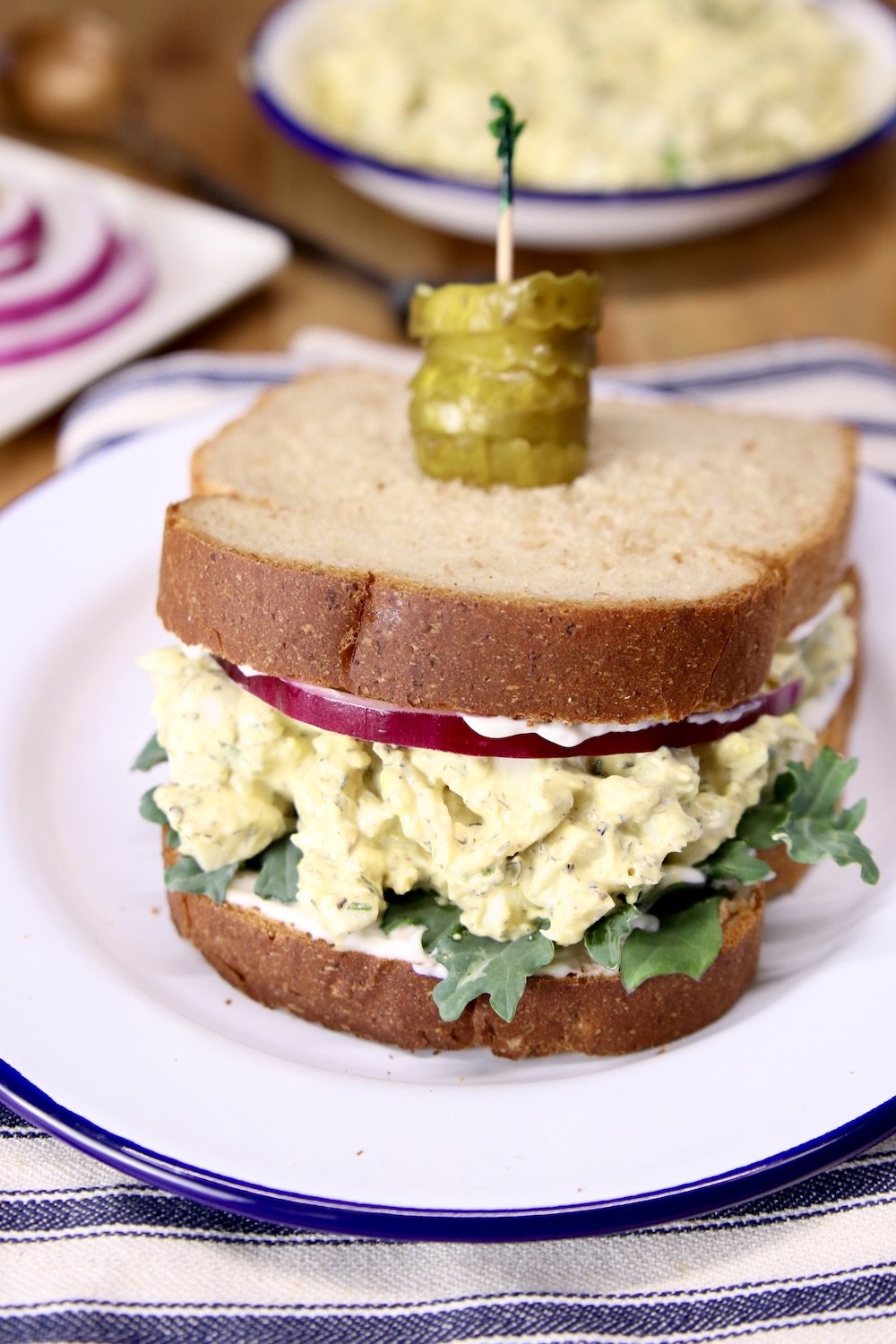 Egg Salad Sandwich on a plate with toothpick and pickles on top