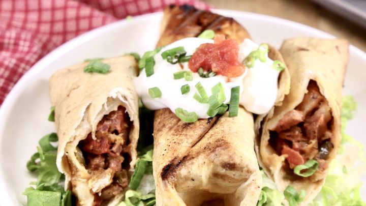 short rib burritos on a plate - one whole, one cut in half, with shredded lettuce, sour cream and salsa