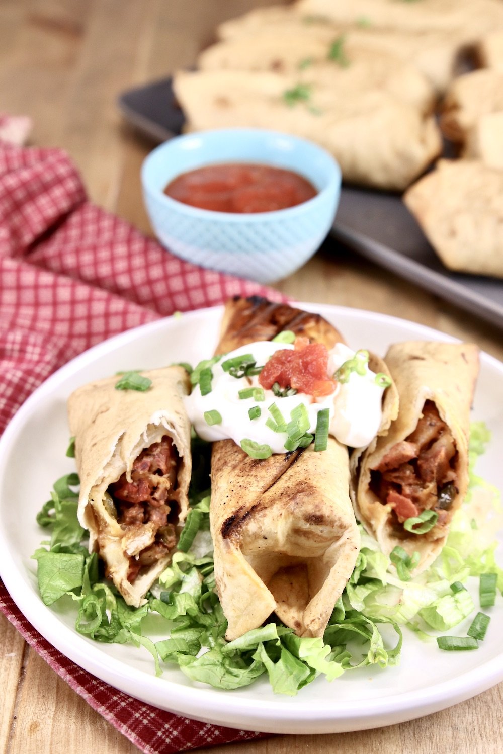Short Rib Burritos on a plate - one whole, one cut in half with filling showing. On a bed of lettuce, topped with sour cream and salsa