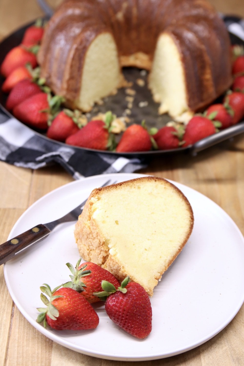 Amaretto Pound Cake - slice on a plate with fresh strawberries and cake on a platter in background