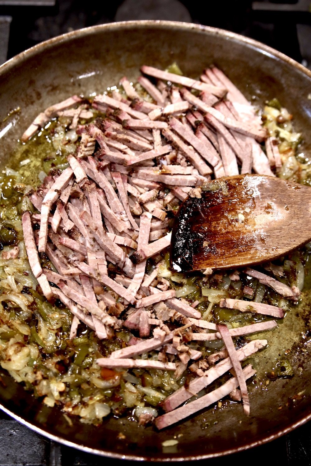 chopped brisket in a skillet with pepper and onions. Wood spoon stirring.