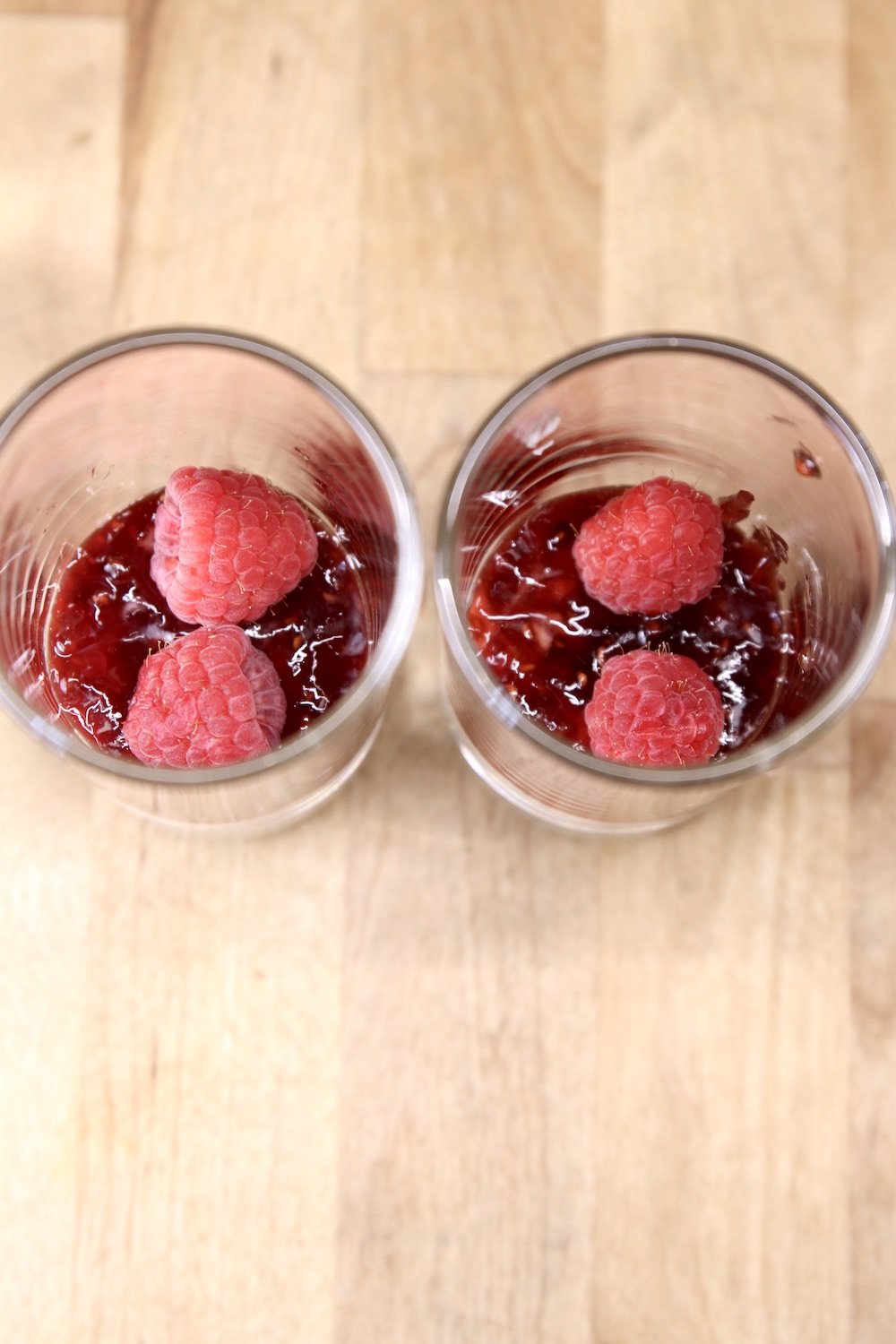 2 dessert glasses with cheesecake filling, raspberry preserves, raspberries