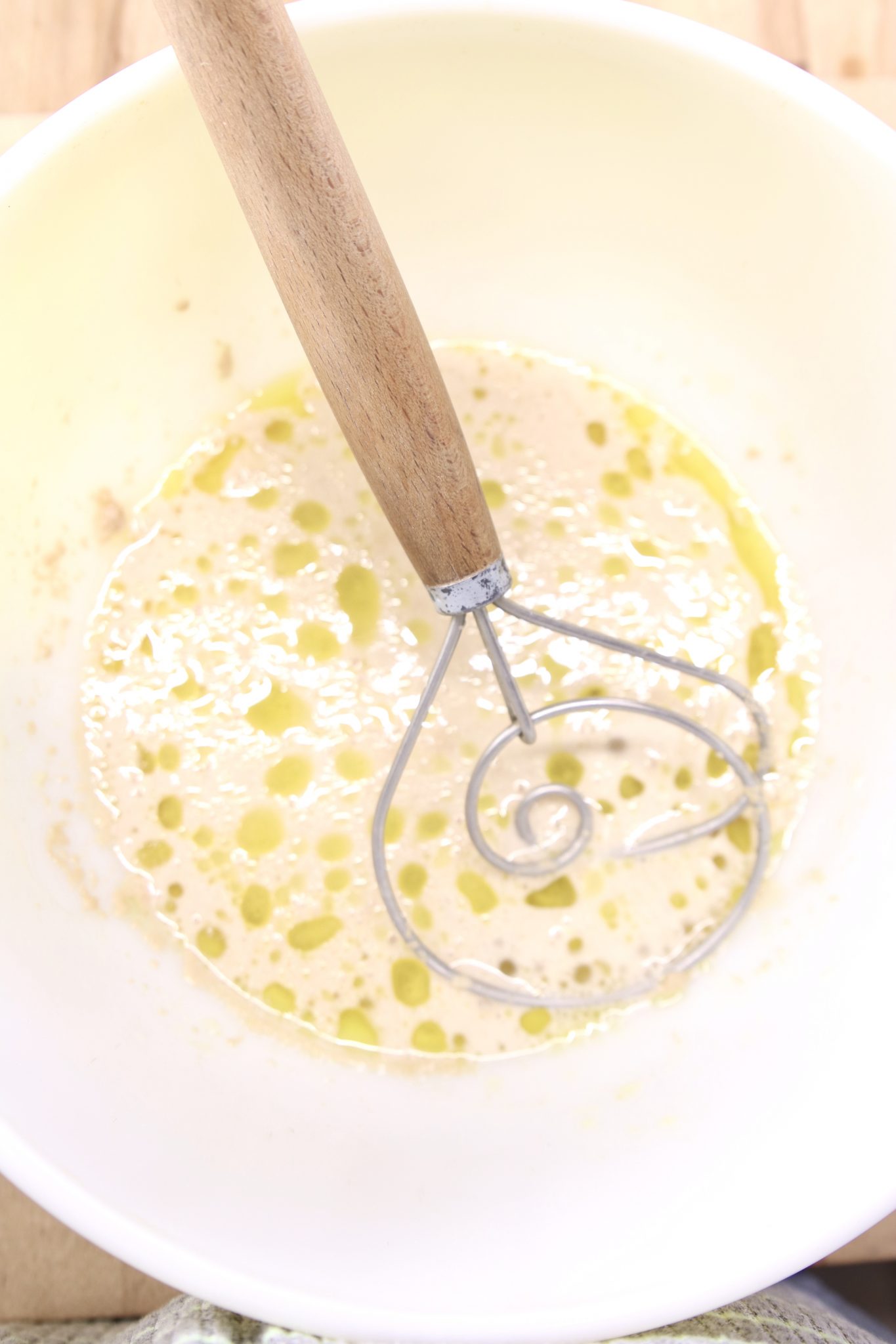 yeast, water, sugar and oil in a bowl with a dough whisk
