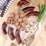 smoked sausage cut into 3 inch pieces with slices in center of cutting board with green onions on the side