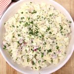 Potato salad in a white bowl, topped with parsley