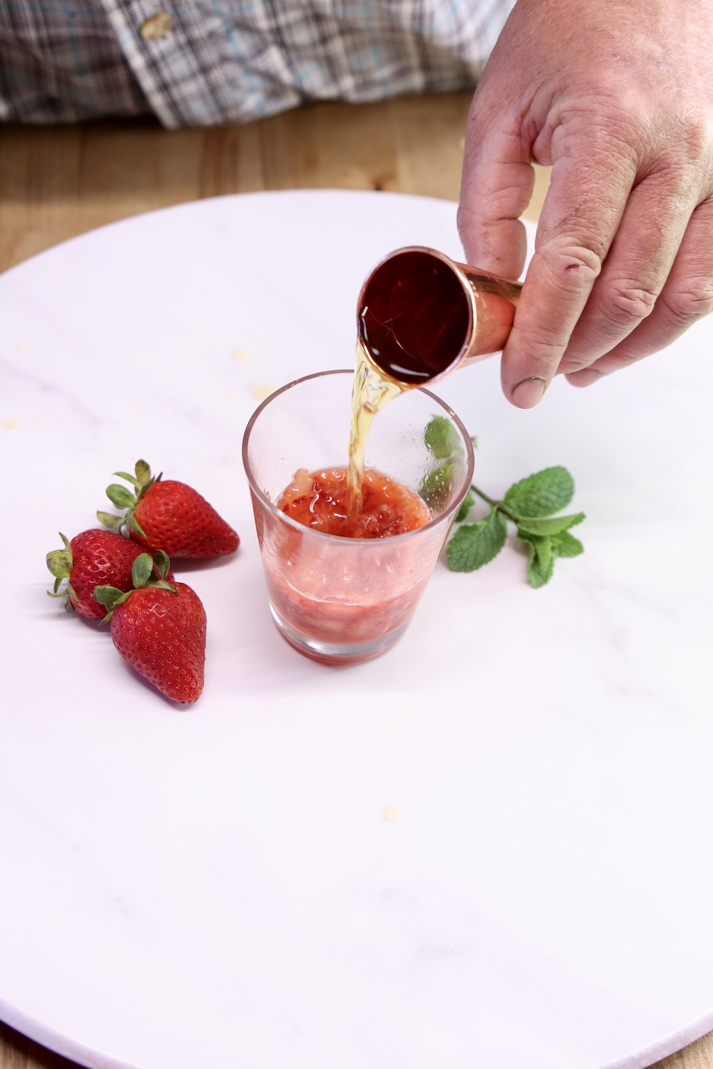 pouring whiskey into a strawberry cocktail glass