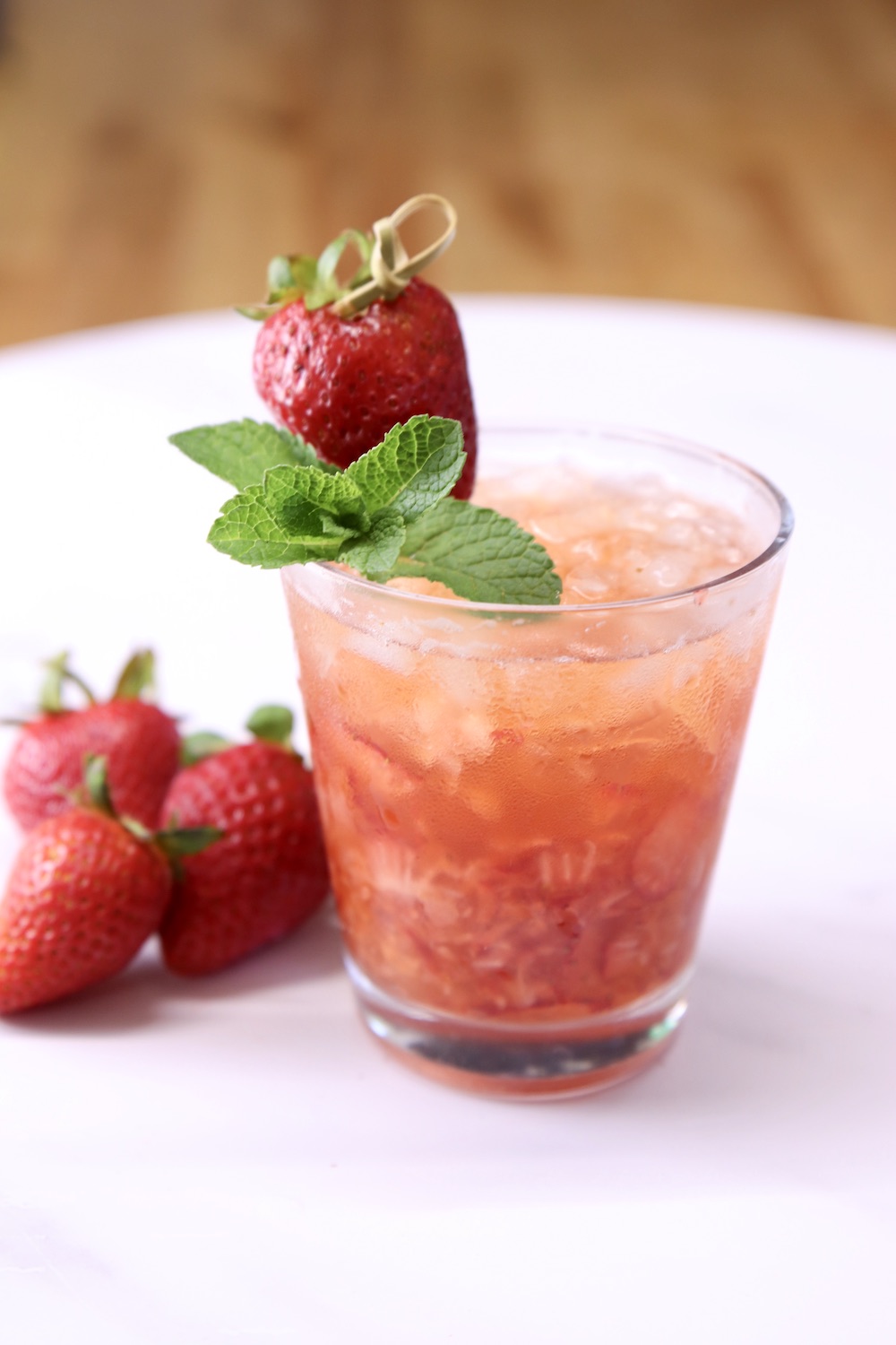 strawberry cocktail in an old fashioned glass with mint and strawberry garnish