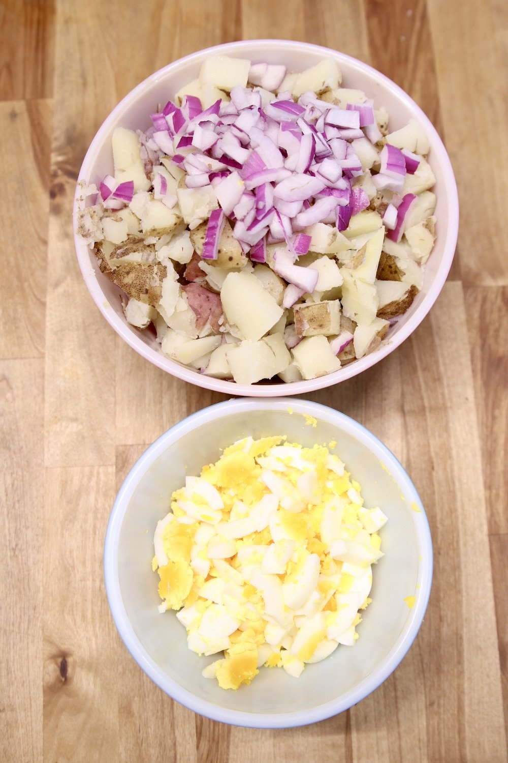 bowl with diced potatoes and red onions, smaller bowl with diced hard boiled eggs