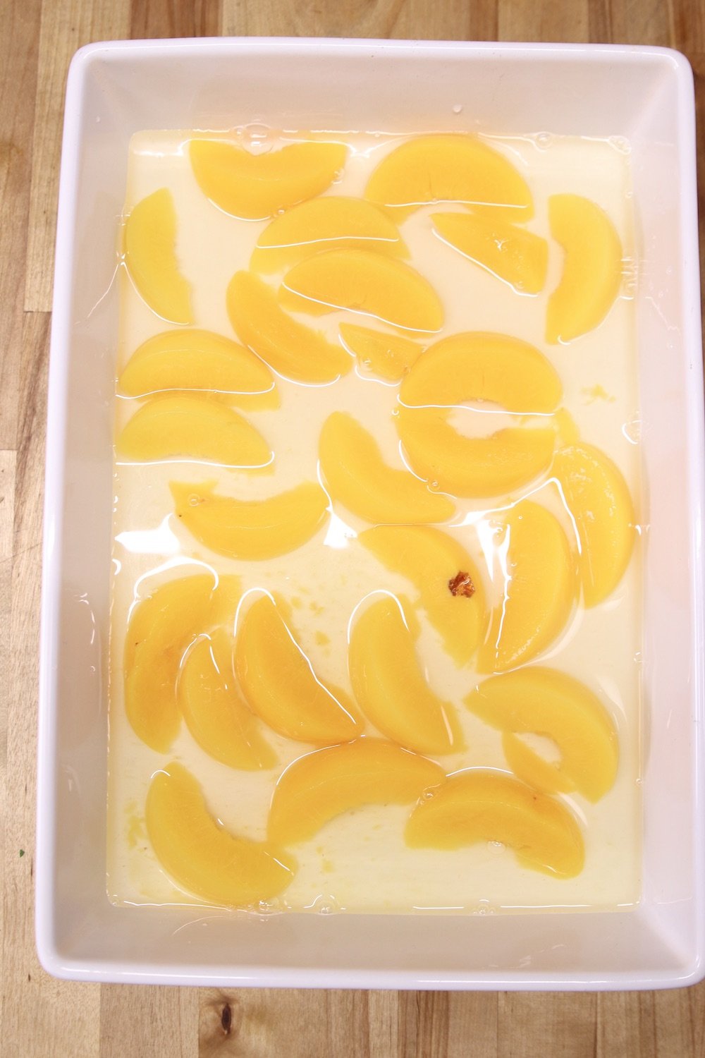 sliced peaches in a white cake pan with syrup