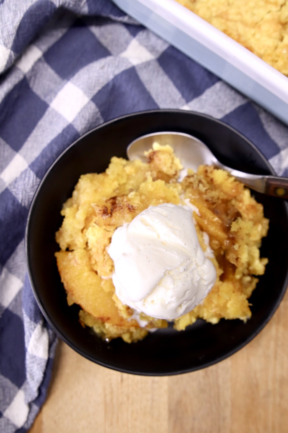 close up of overhead view of peach dump cake and vanilla ice cream in a bowl