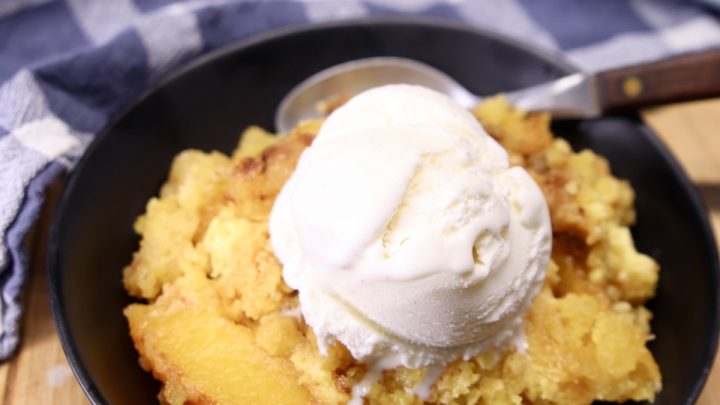 Peach Dump Cake served in a black bowl, topped with vanilla ice cream