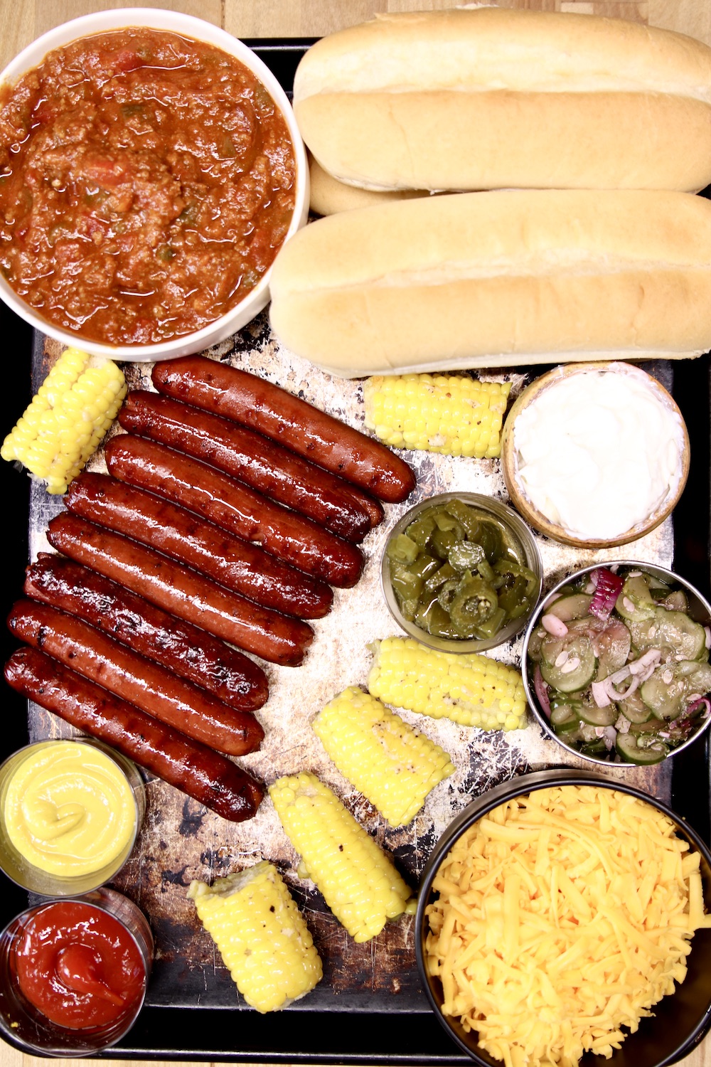 tray of grilled hot dogs, chili, buns, cheese, condiments for chili cheese dogs