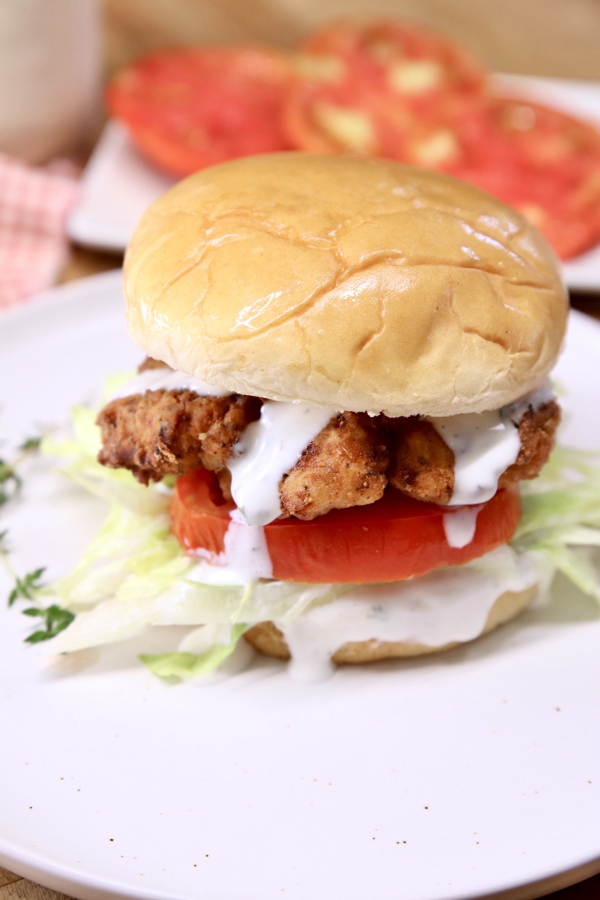 fried chicken sandwich with lettuce, tomato and ranch dressing drizzle