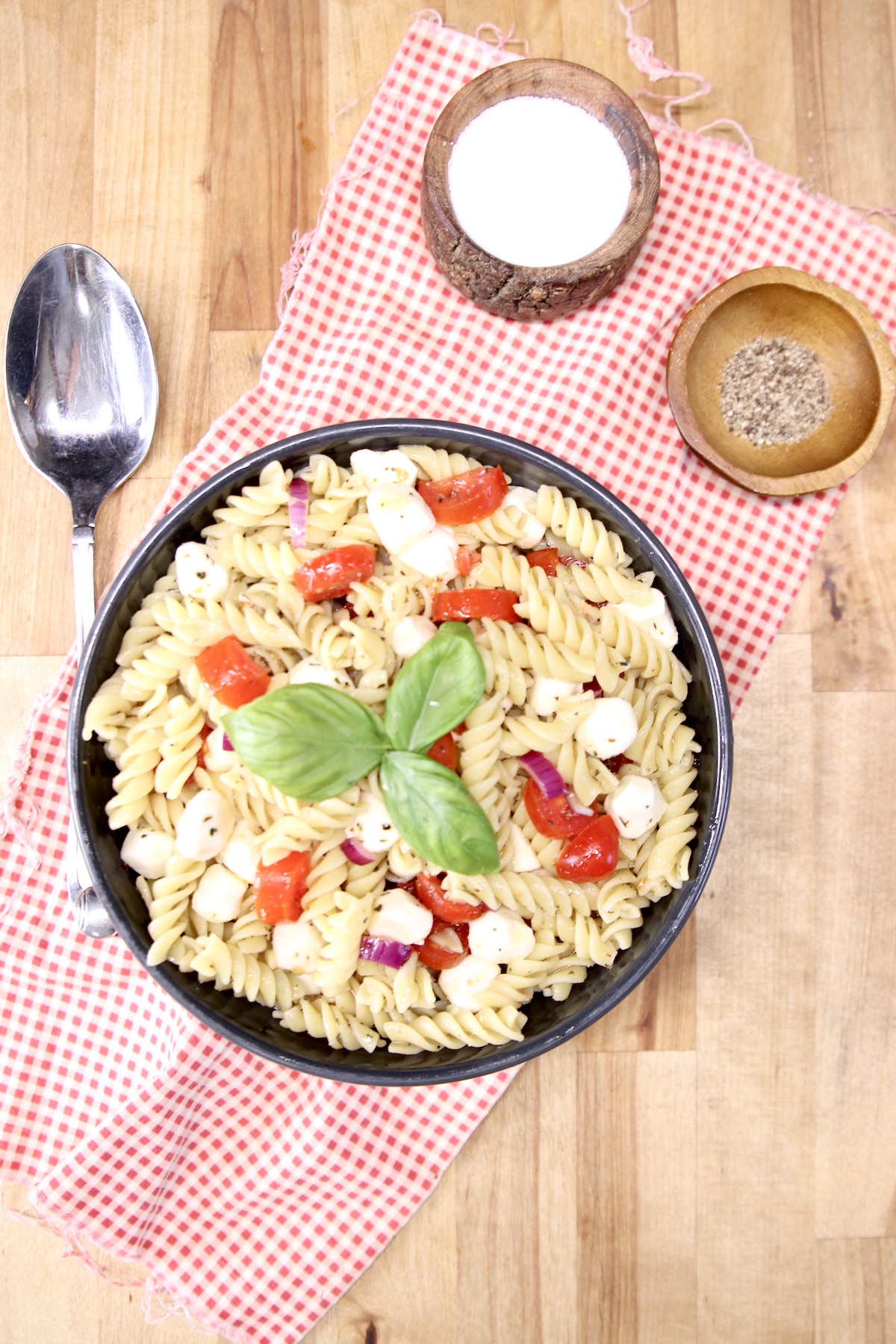 Pasta salad with tomatoes and basil , bowl of salt and pepepr