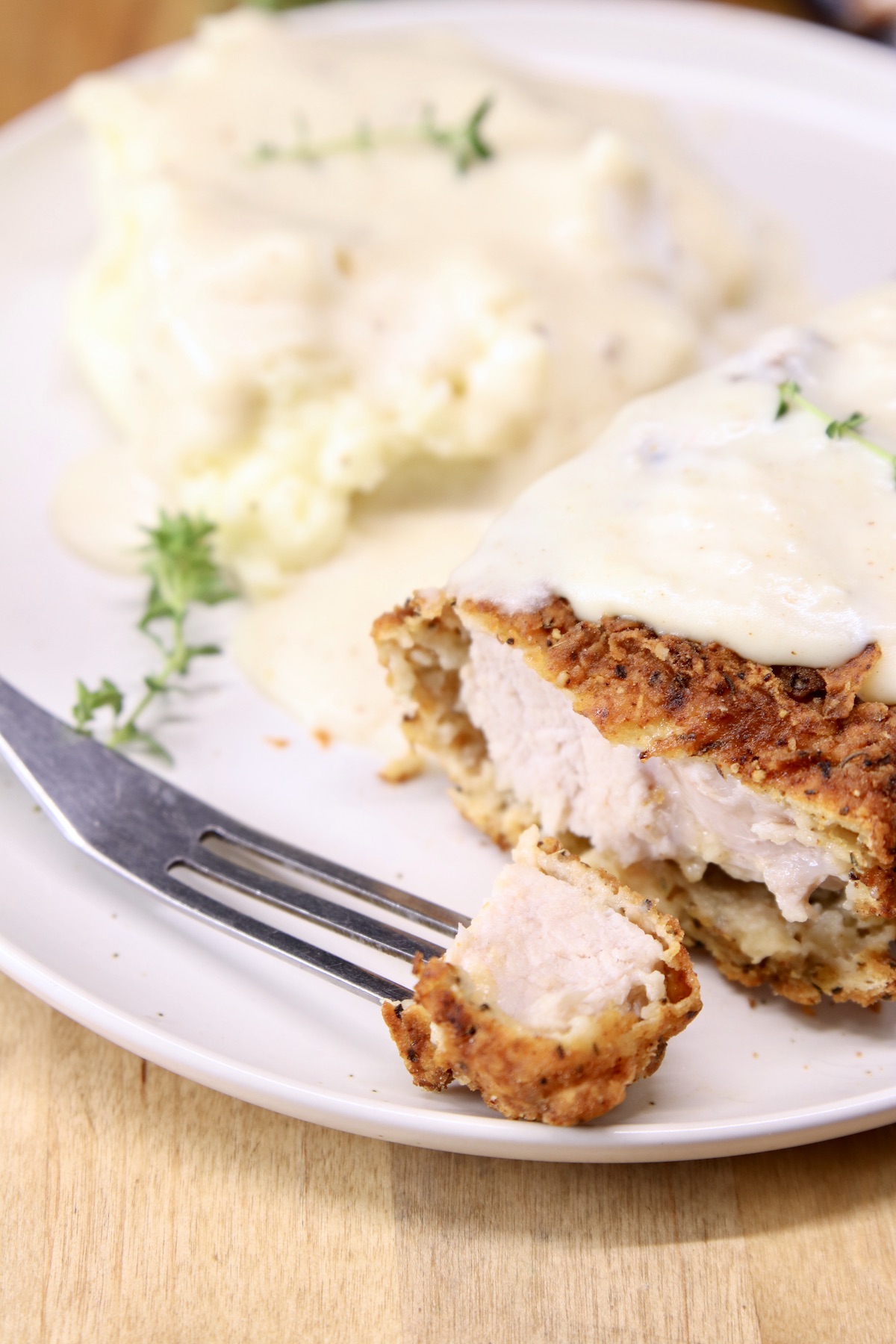 fried pork chops bite on a fork, plate with mashed potatoes and gravy