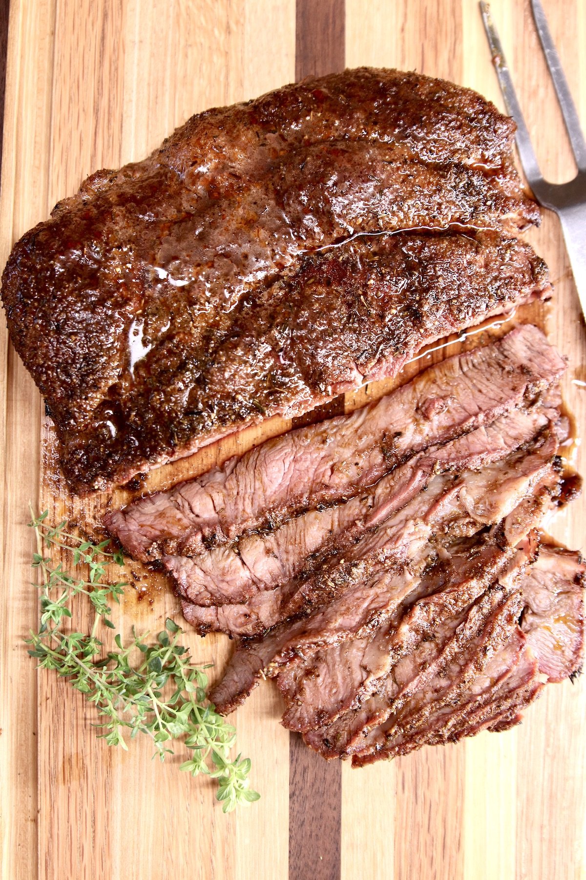 chuck roast on a cutting board with fresh thyme, partially sliced
