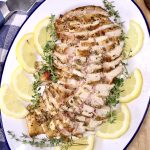 sliced chicken breast on a platter with lemon slices and thyme garnish