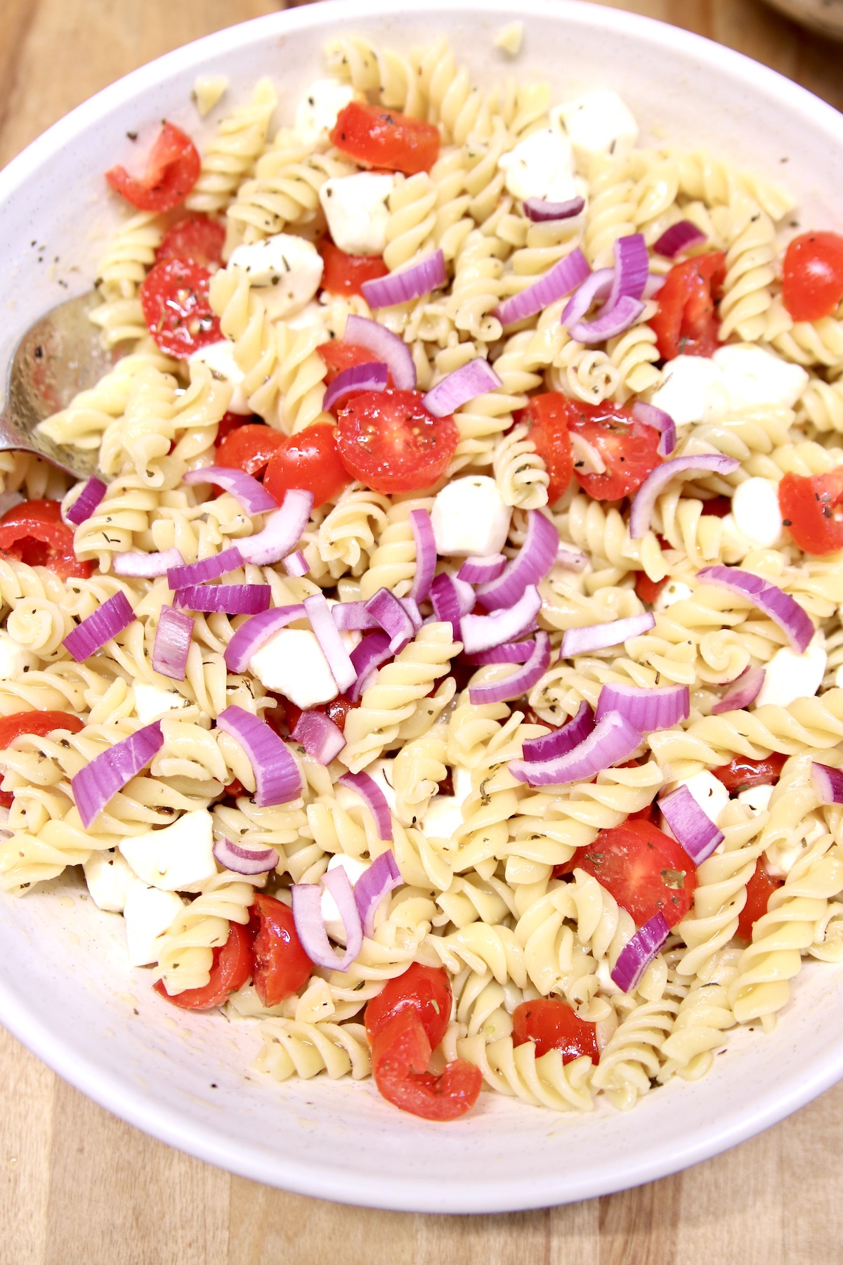 rotini pasta in a bowl with sliced tomatoes, red onion and mozzarella balls