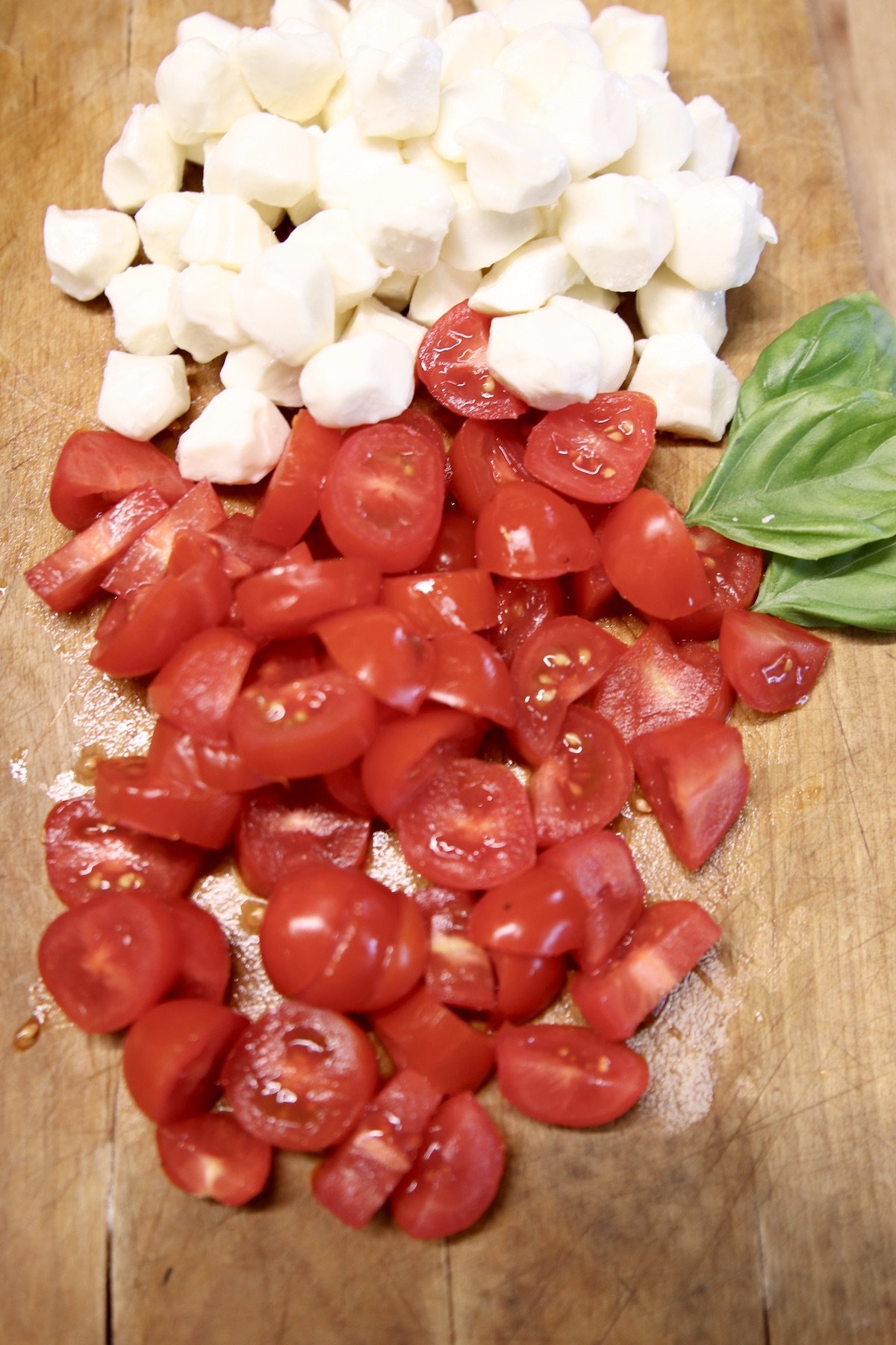 mozzarella balls, sliced cherry tomatoes and basil leaves on a cutting board