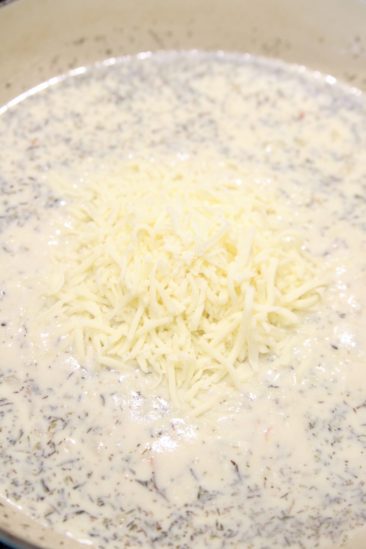 adding shredded mozzarella to creamy sauce for pasta