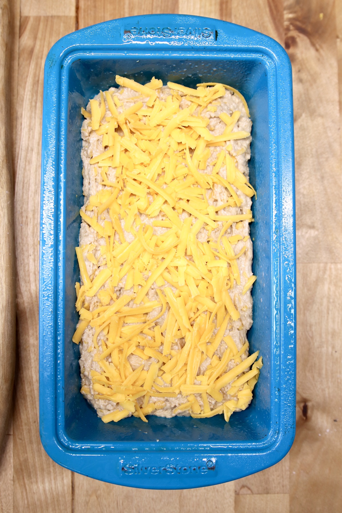 cheddar cheese sprinkled over beer bread batter in a blue loaf pan