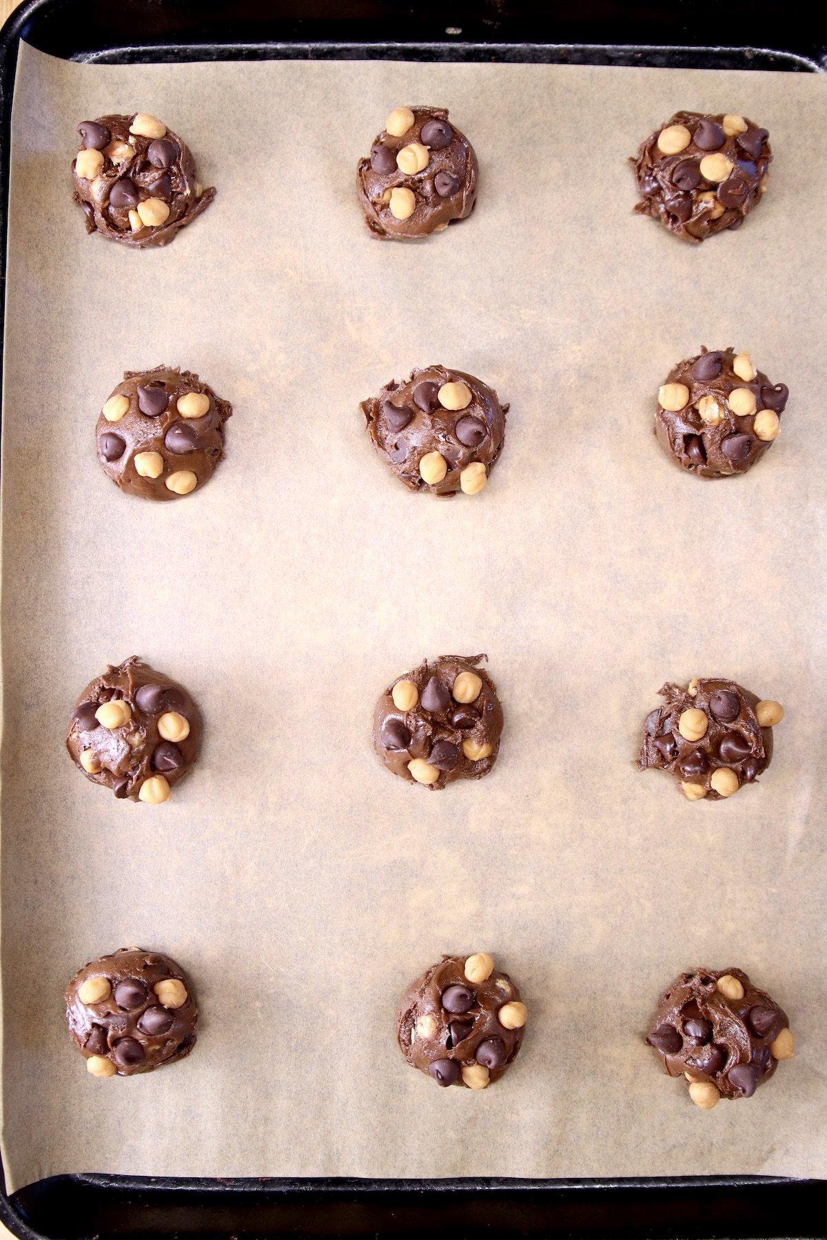 cookie dough balls with chocolate chips and caramel bits on a parchment lined baking sheet