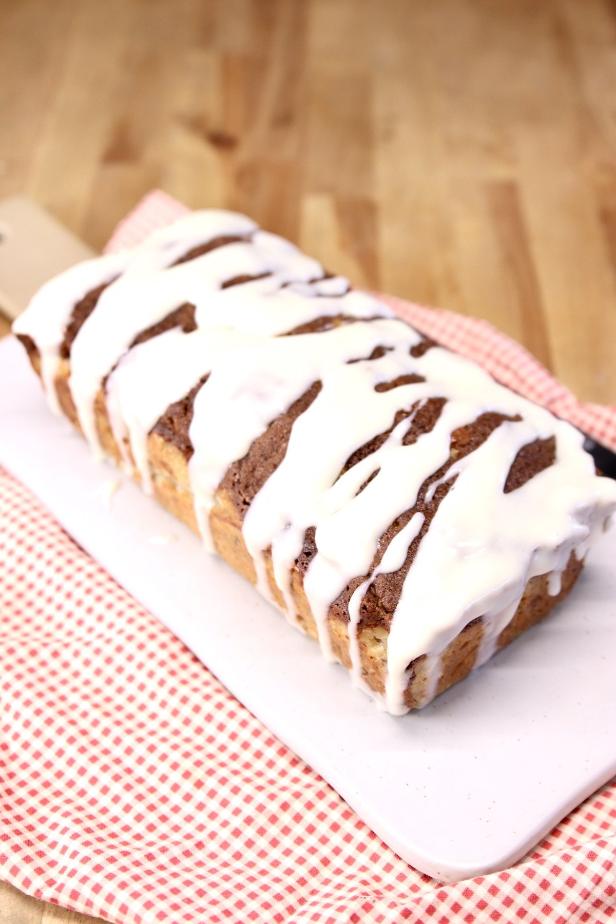 apple bread with cream cheese drizzle on a serving board, red check napkin under the board