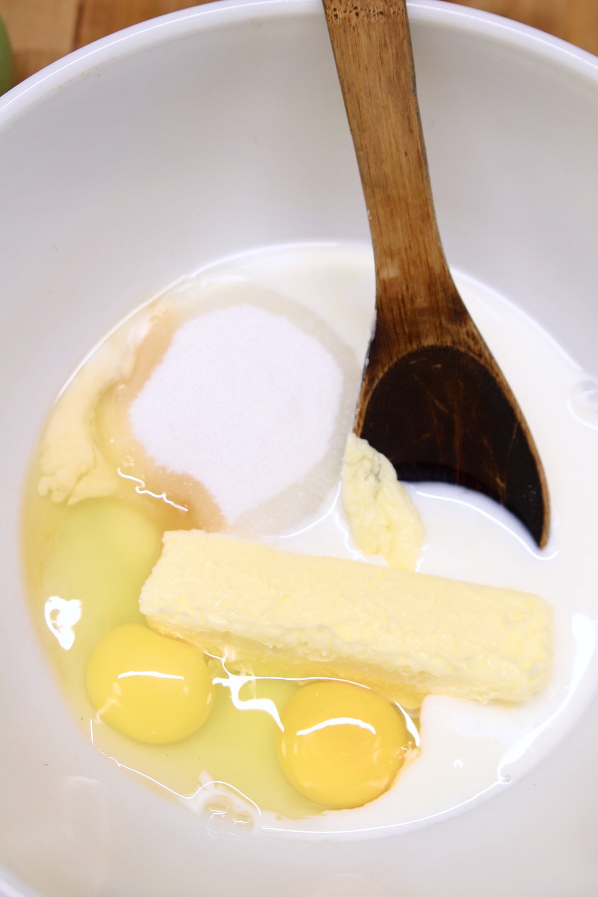 bowl with eggs, butter, sugar, milk, vanilla, wood spoon