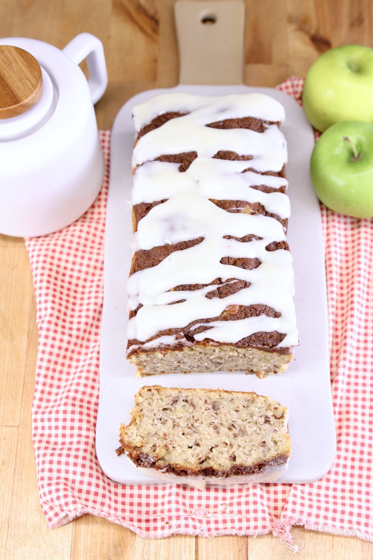 board with apple bread, once slice off of the end, tea pot, 2 apples