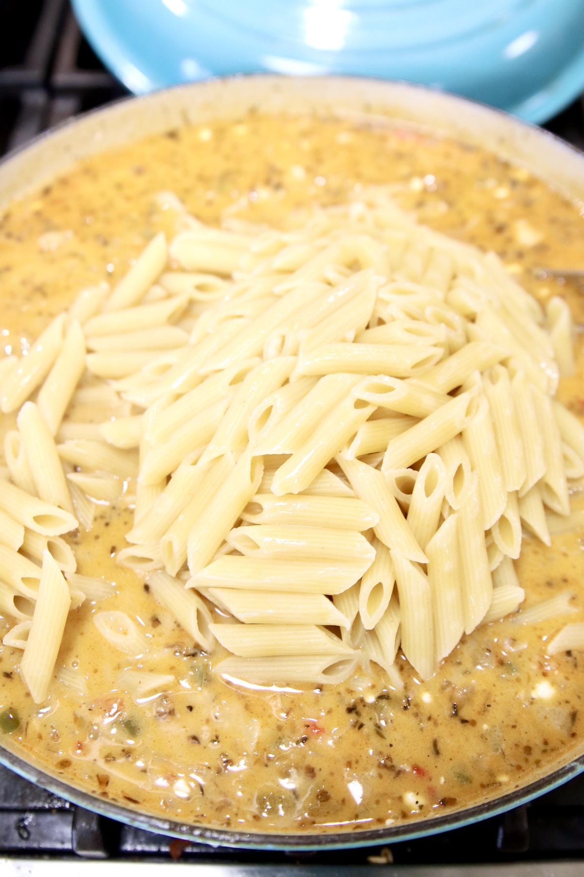 adding penne pasta to cheesy sauce in a pan