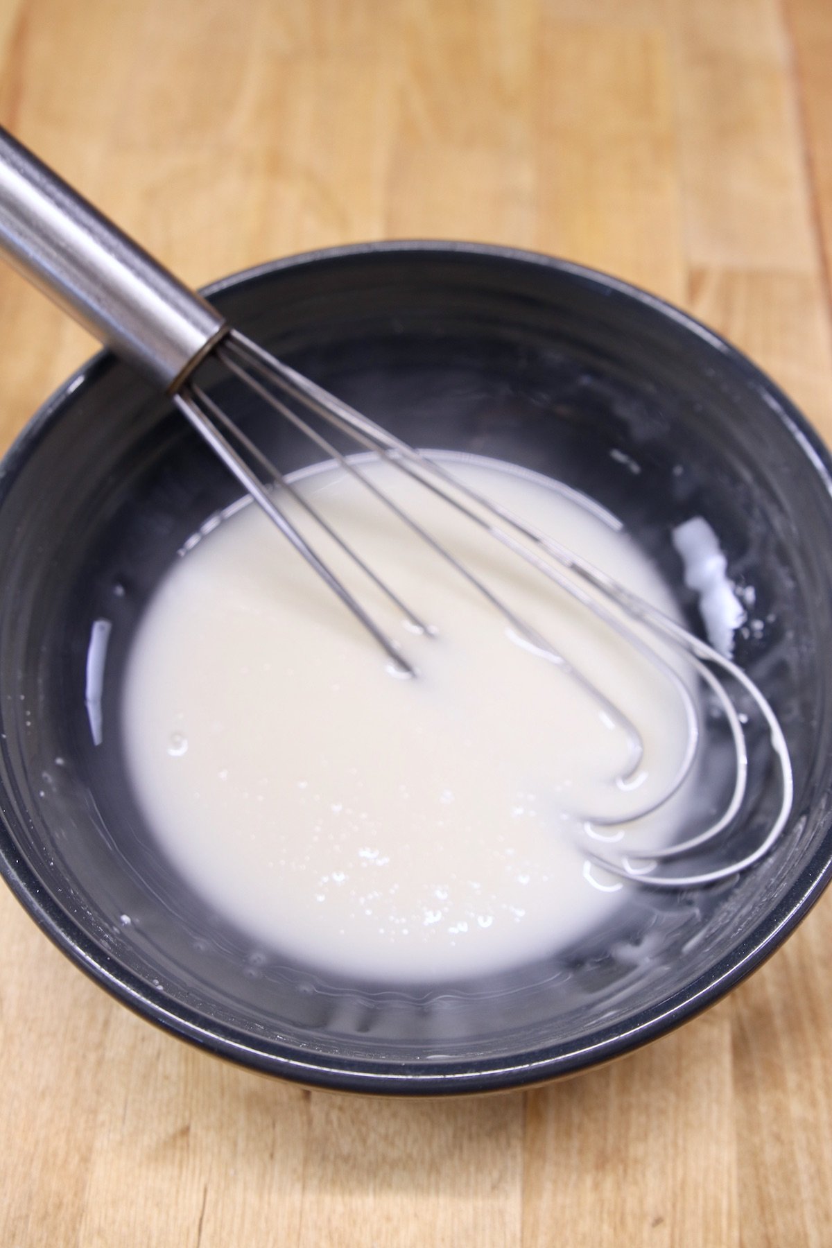 whisk in a black bowl with powdered sugar glaze