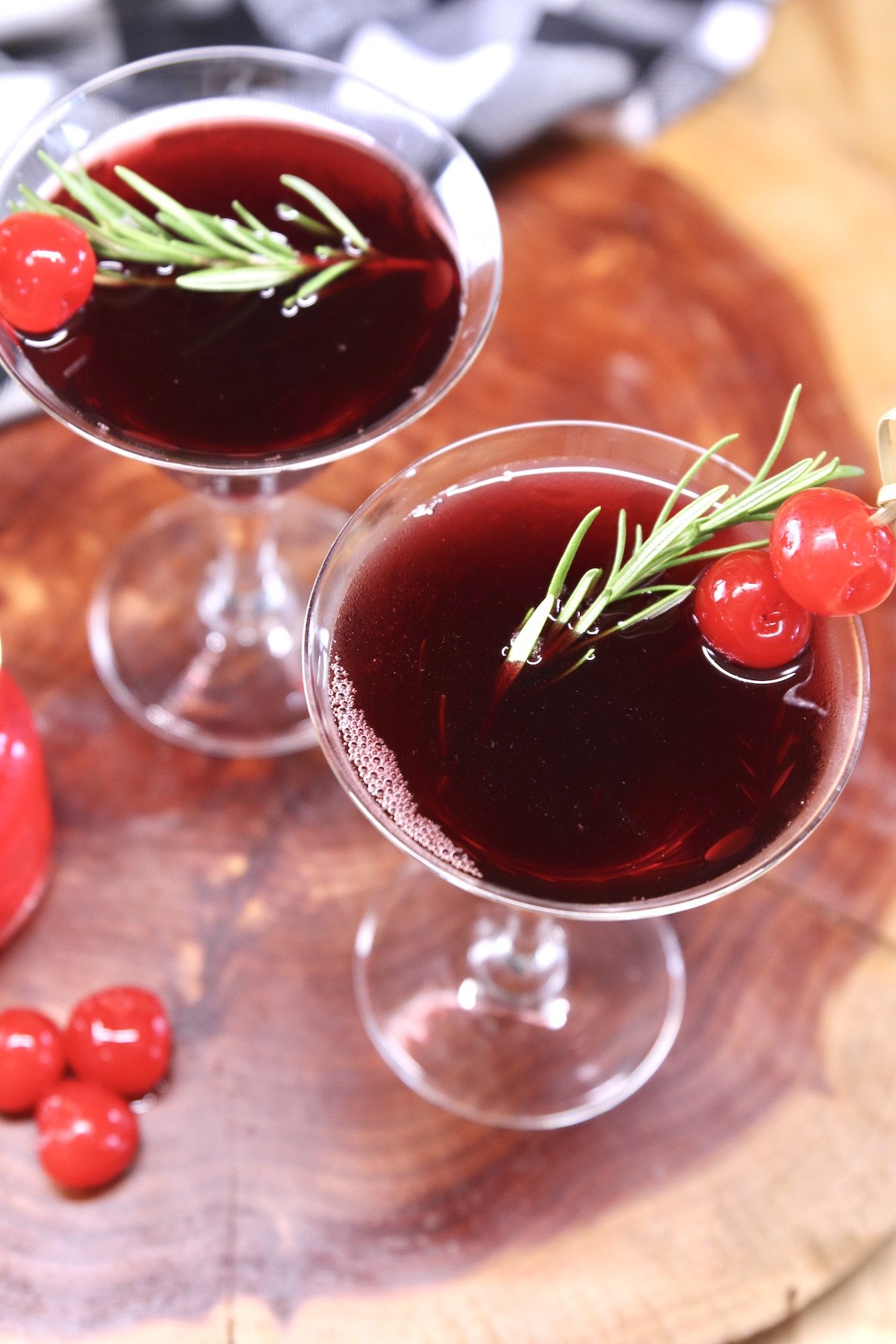 overhead of 2 cranberry wine cocktails with rosemary and maraschino cherry garnish