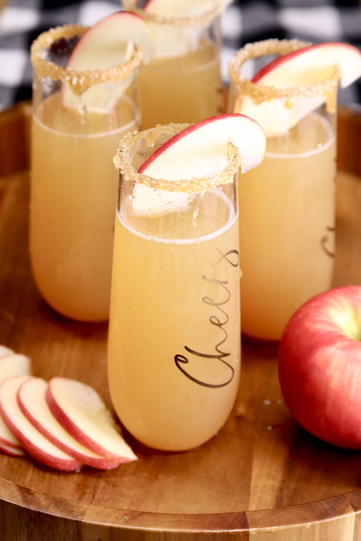 Apple Cider Mimosas with apple garnish on a wood tray with sliced apples