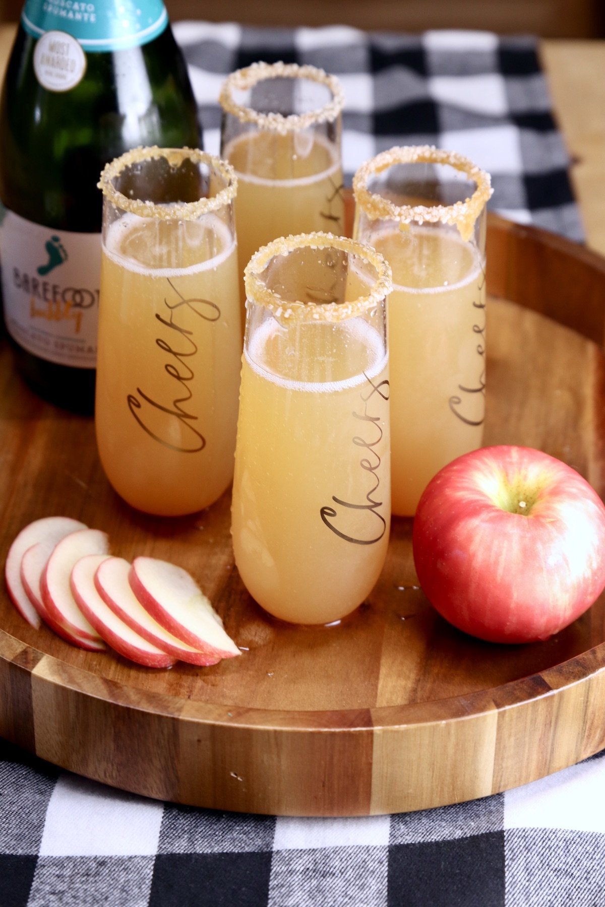 tray of apple cider mimosas with sparkling wine bottle, sliced apples and whole apple