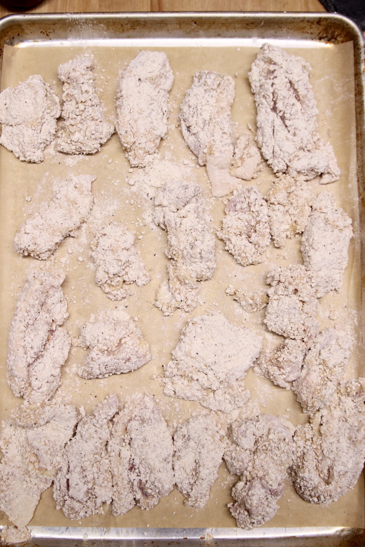parchment lined baking sheet with breaded chicken for frying