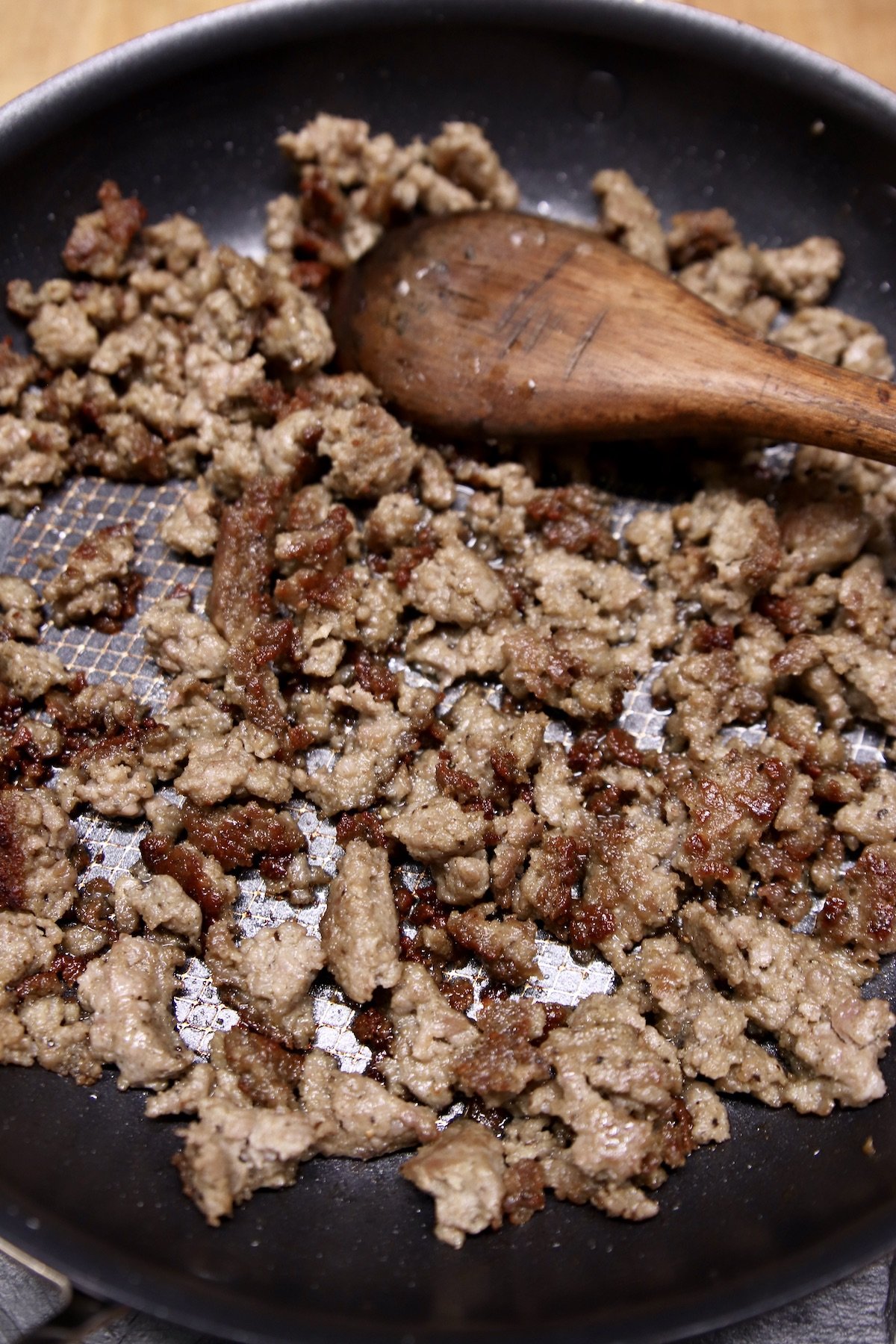 cooked ground sausage in a skillet with wooden spoon