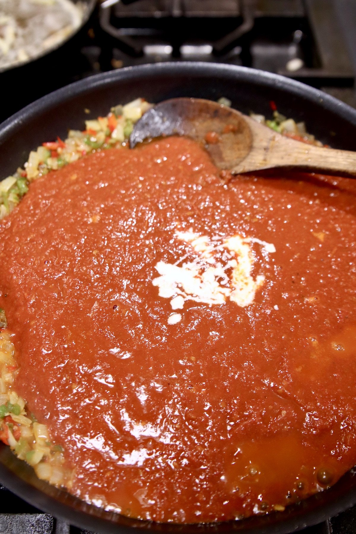 tomato sauce and heavy cream added to a skillet of cooked onions and peppers