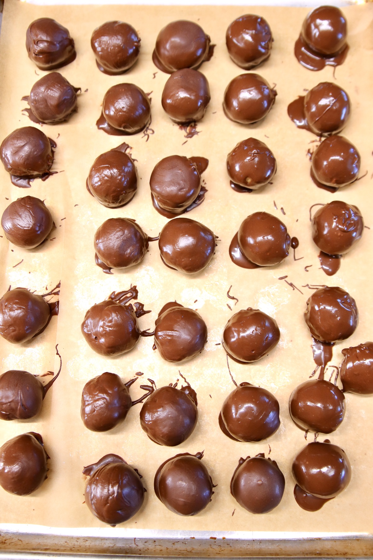 chocolate dipped peanut butter balls on a sheet pan lined with parchment