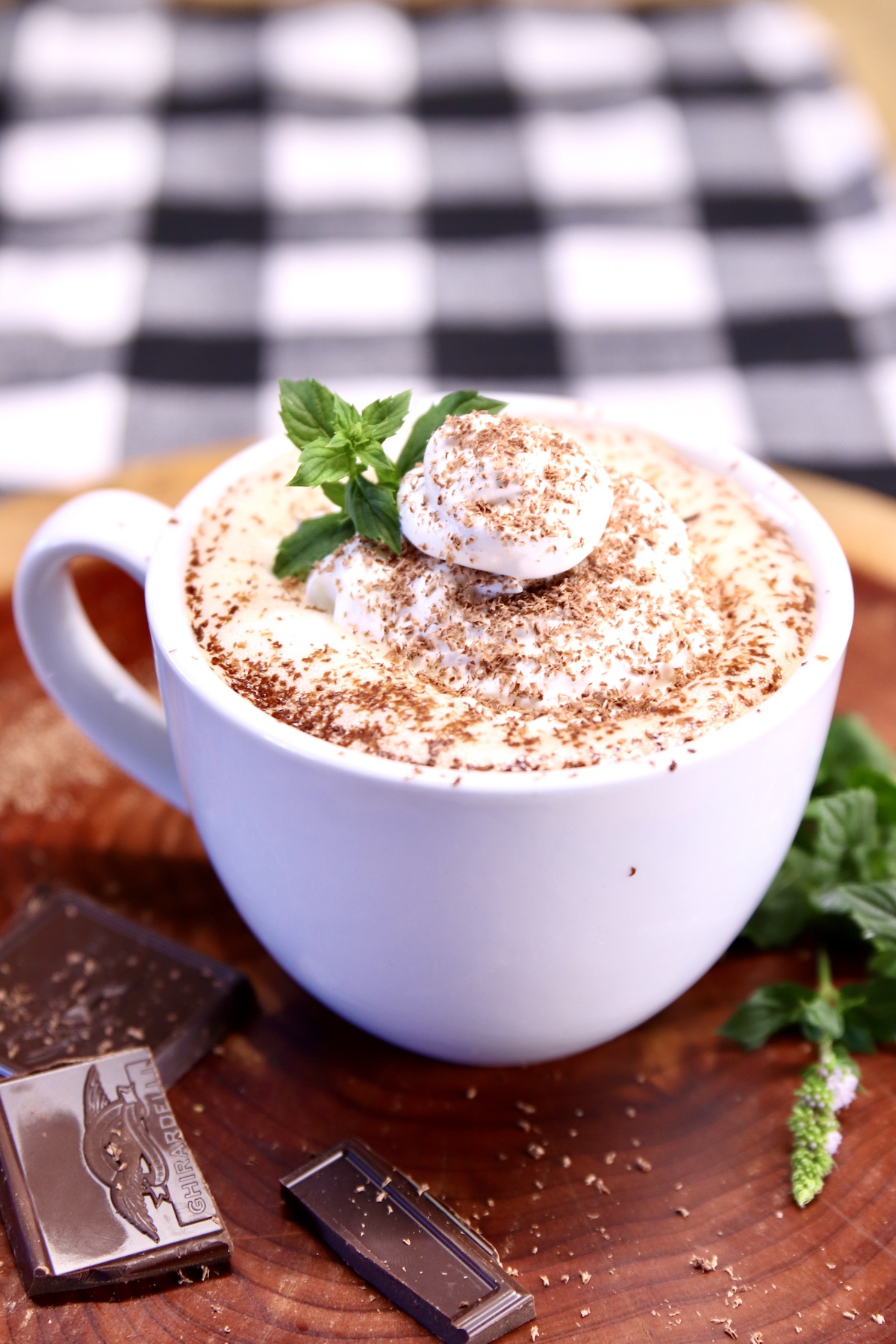 peppermint hot cocoa in a mug on a wood board with chocolate squares, fresh mint