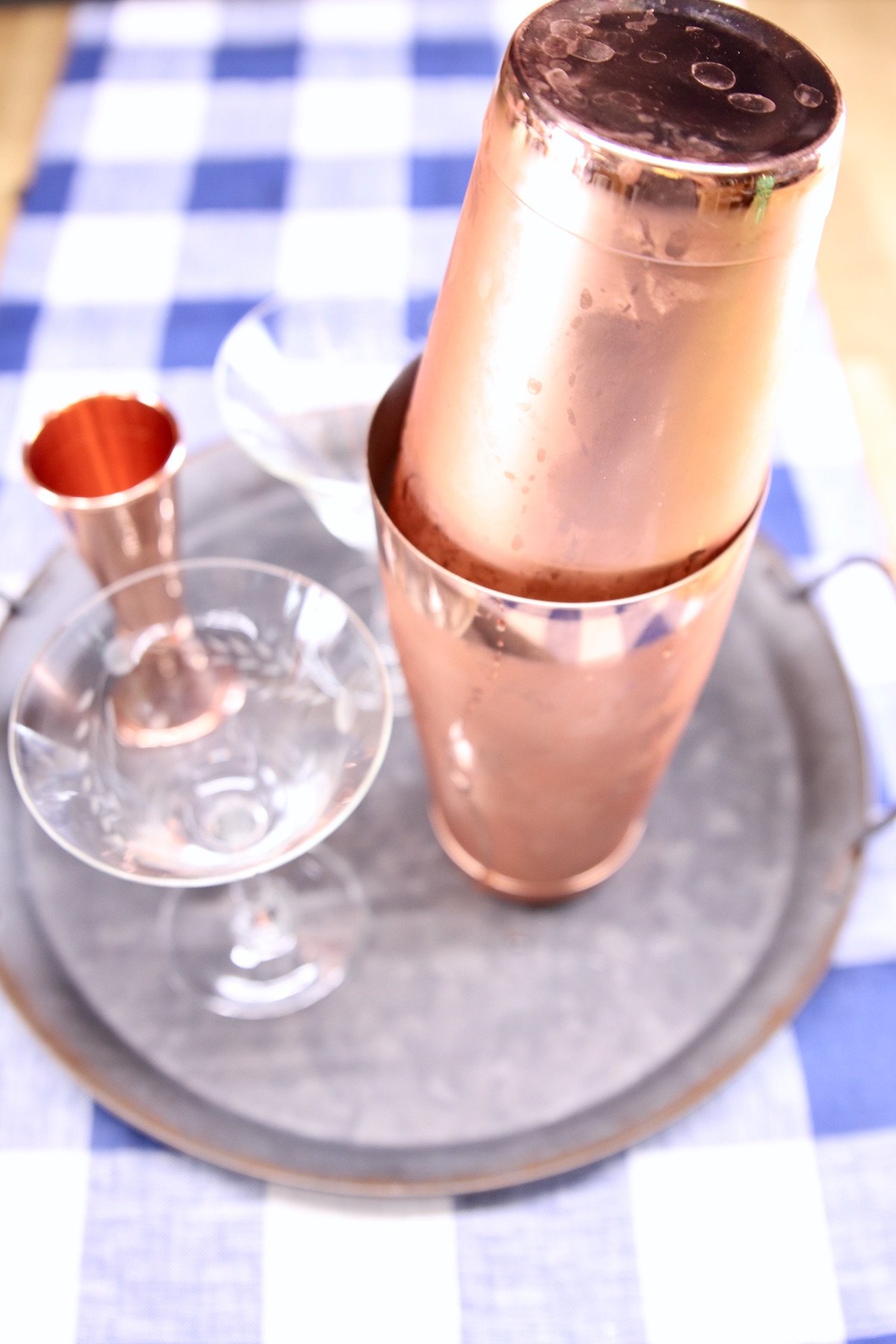 copper cocktail shaker with coupe glass on a tray