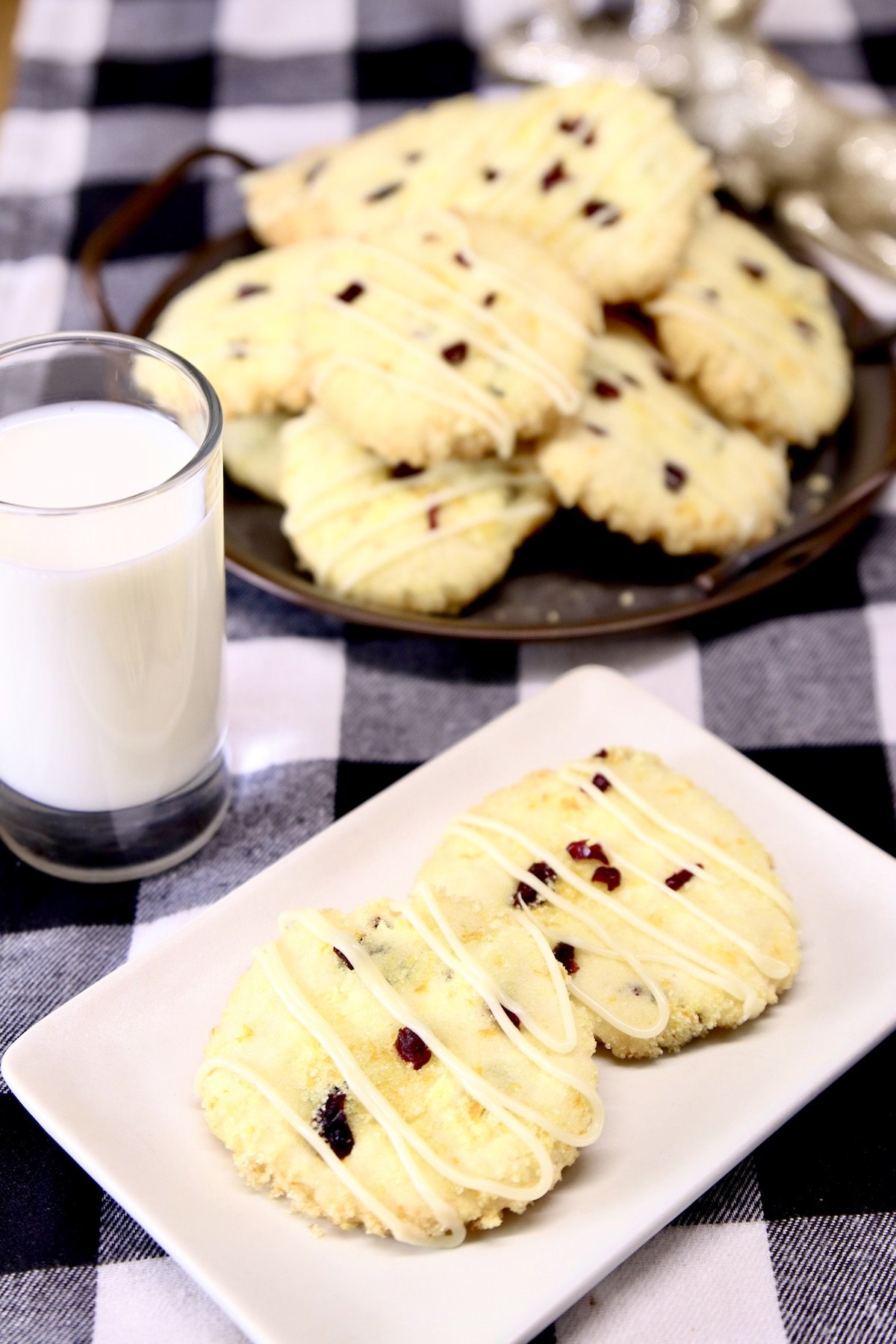 plate with 2 cranberry cookies, glass of milk, platter of cookies
