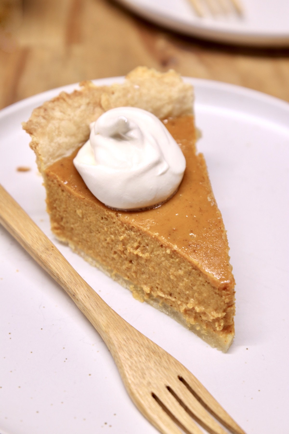 Pumpkin pie with cool whip slice on a plate, bamboo fork