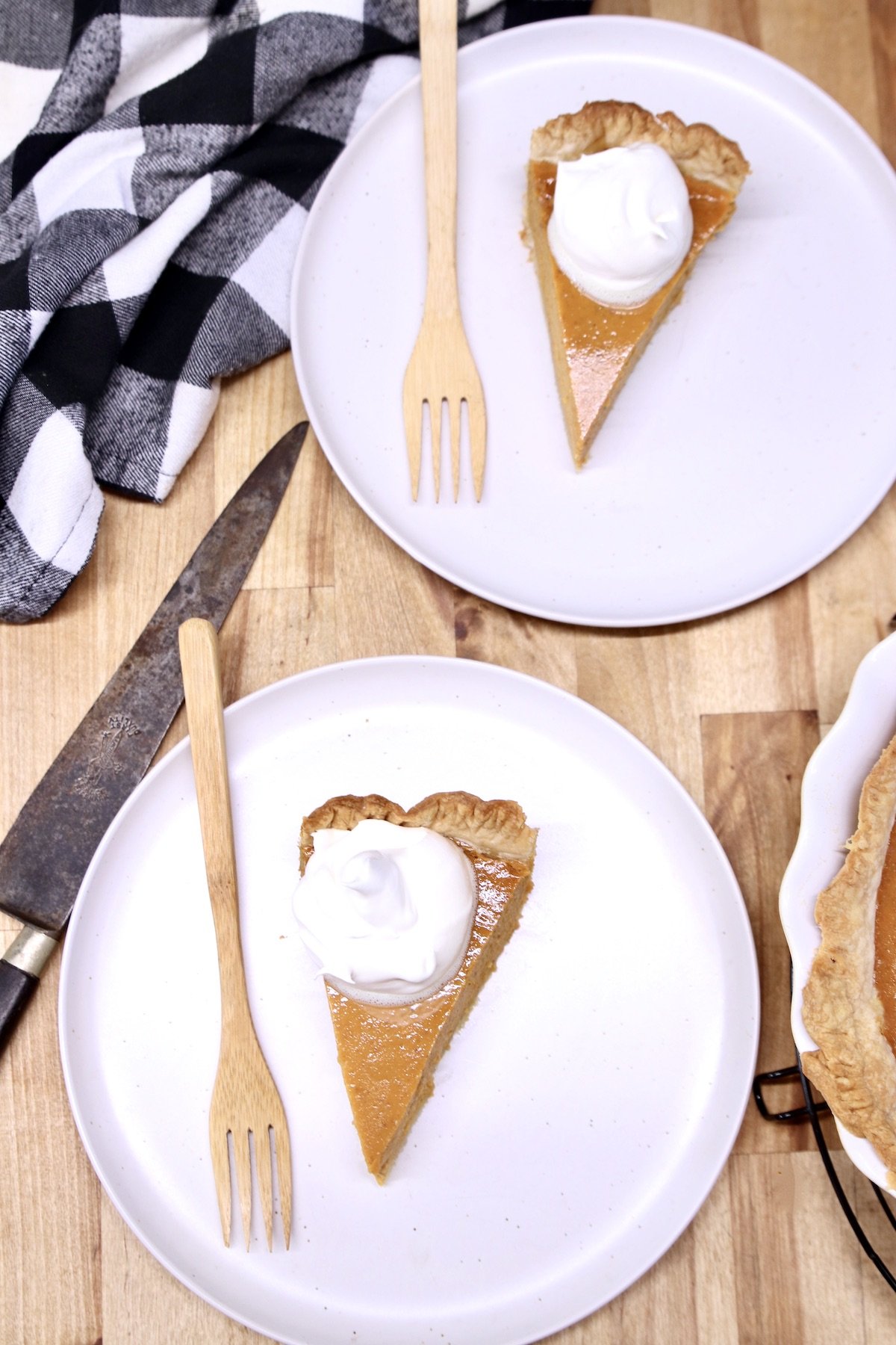 overhead of 2 slices of pumpkin pie with cool whip on white plates with bamboo forks