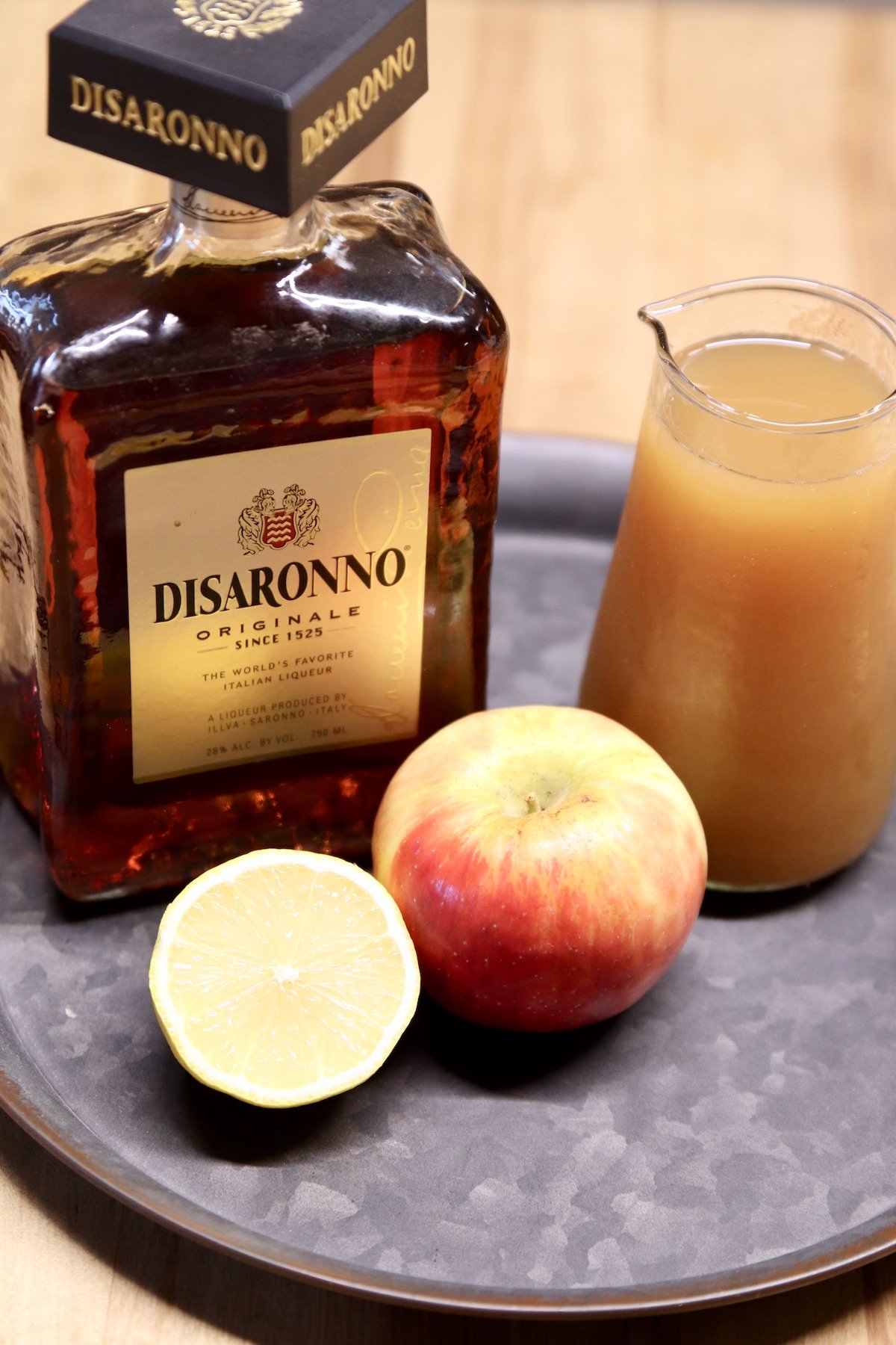 Disaronno liqueur, apple cider, half a lemon and an apple on a tray