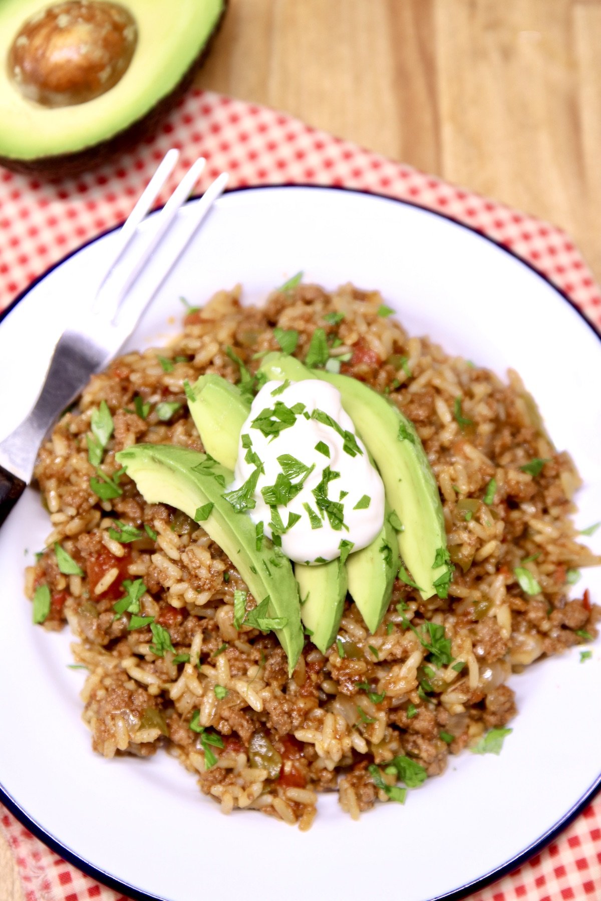 close up of plate of Spanish Rice topped with avocado and sour cream, half avocado to the side