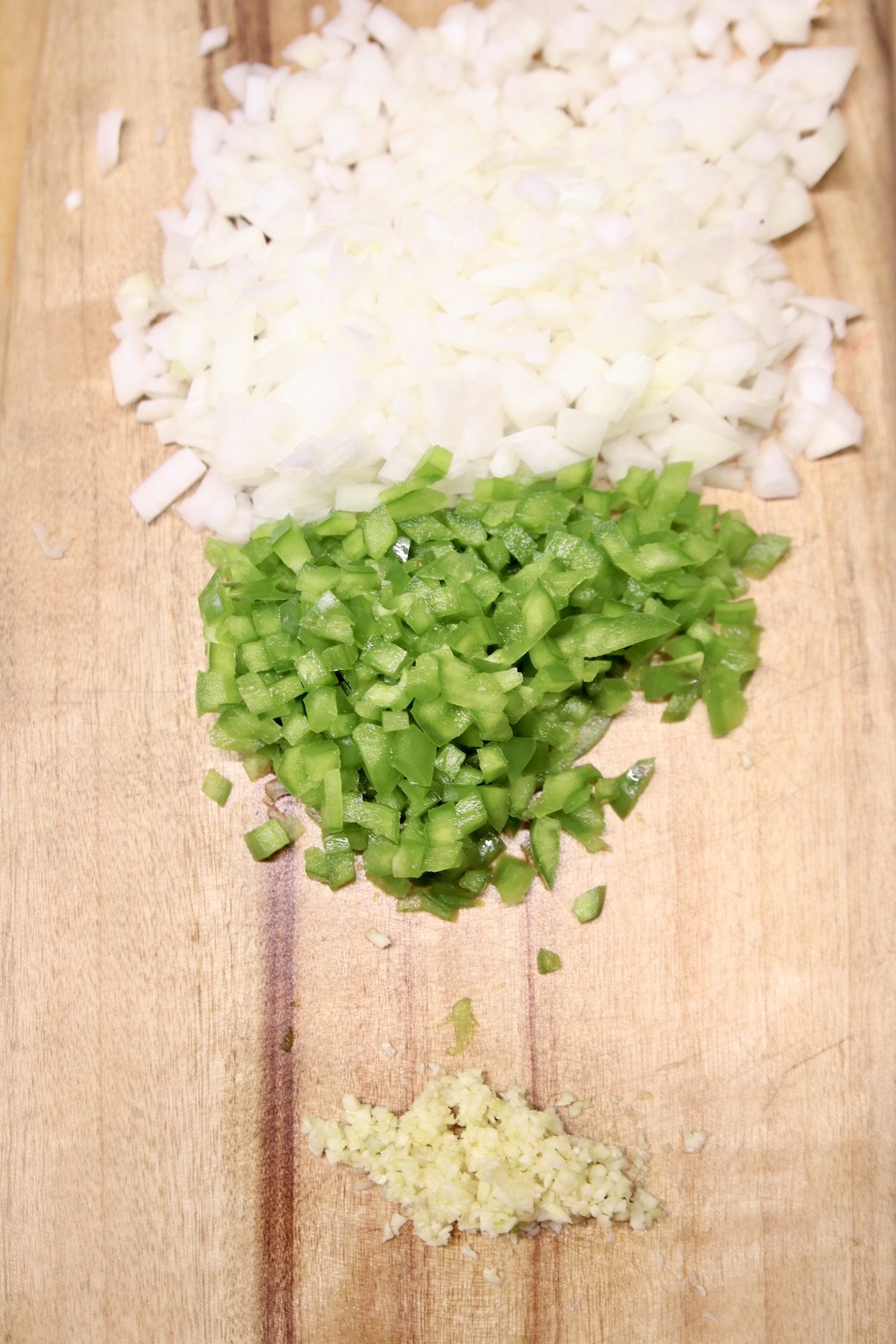 diced onions, bell peppers and minced garlic on a cutting board