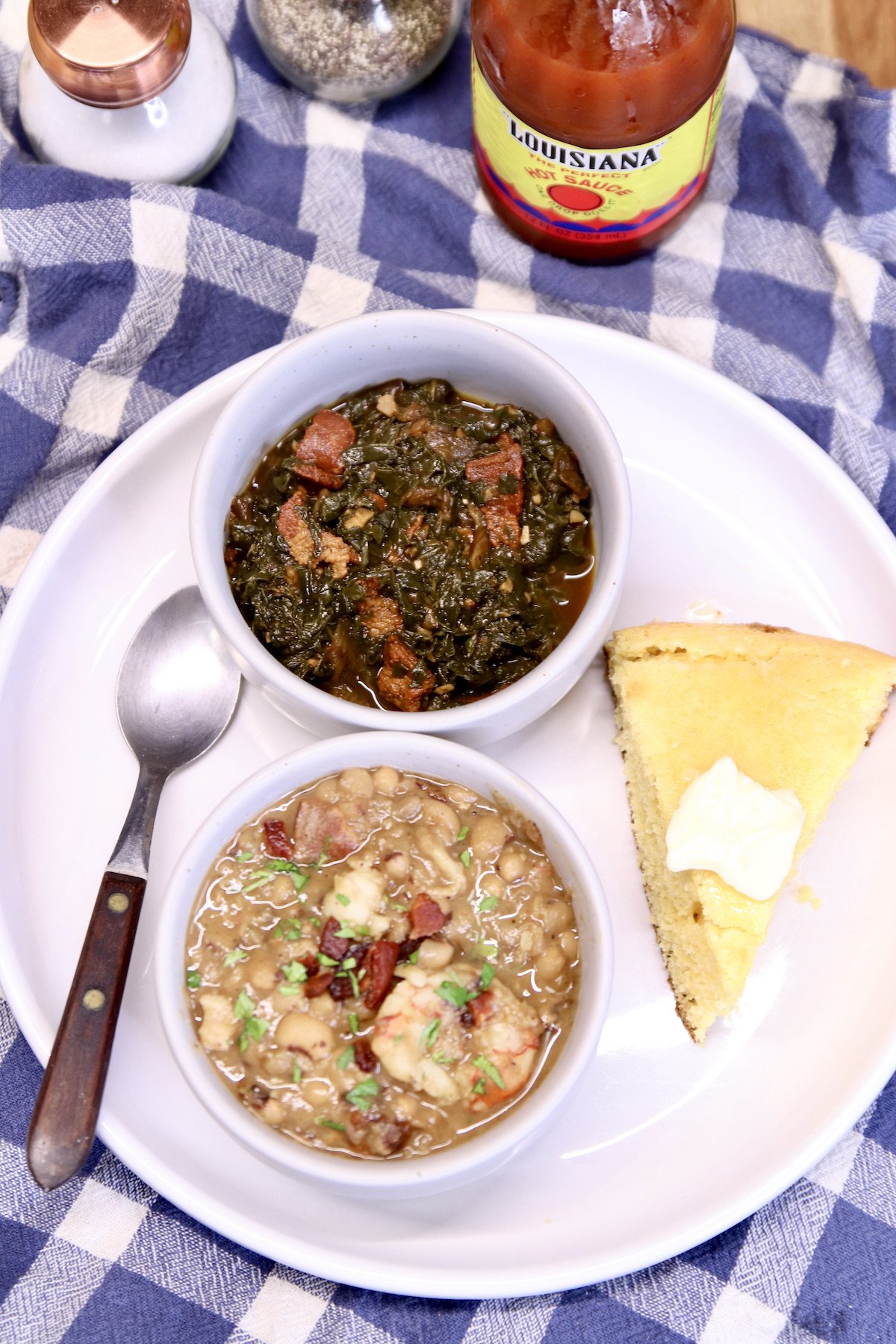 plate with bowl of black eyed peas, bowl of greens and cornbread with a spoon